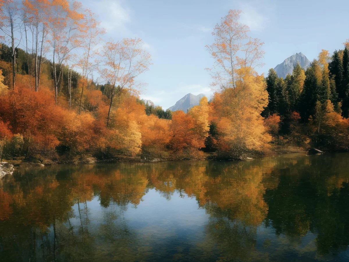 A tranquil lake reflecting vibrant autumn foliage and towering mountains, captured in vivid fall colors.